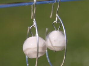 il s'agit d'une paire de boucles d'oreilles forme creole avec une perle de verre blanche