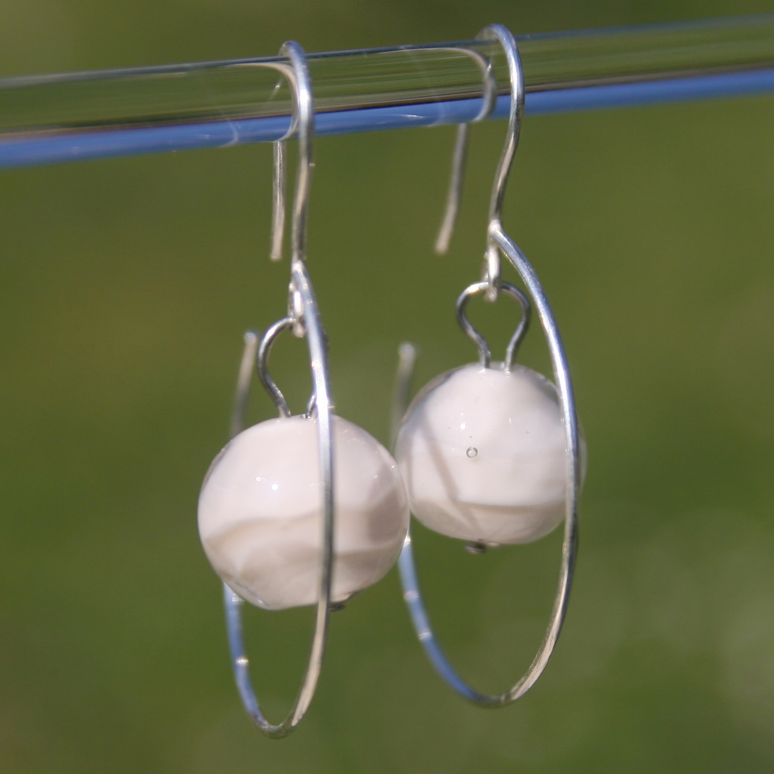 il s'agit d'une paire de boucles d'oreilles forme creole avec une perle de verre blanche